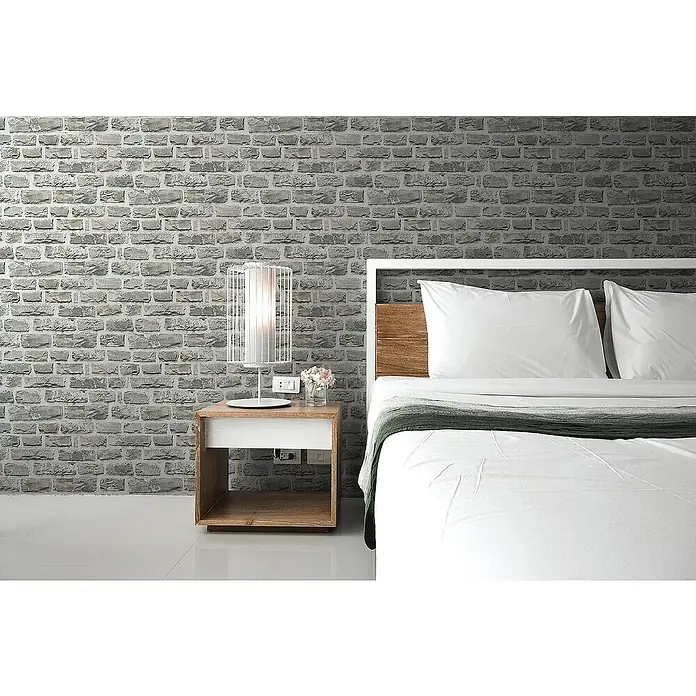 Tadessi Vliestapete M1-No.2635 - Grau, Steinoptik, 10,05 x 0,53 m - Ein modernes Schlafzimmer mit einem Bett mit weißer Bettwäsche, einem Nachttisch aus Holz mit einer weißen Lampe, vor einer grauen Ziegelwand.