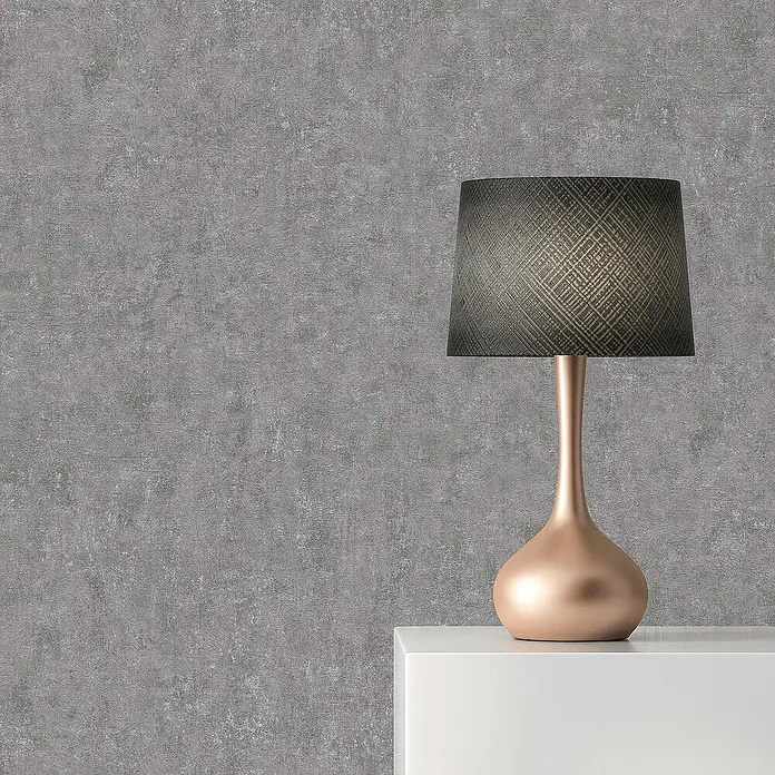 Tadessi Vliestapete M1-No.1813 - Grau, Steinoptik, 10,05 x 0,53 m - Moderne Tischlampe mit roségoldenem Fuß und dunklem gemustertem Lampenschirm auf weißer Konsole vor einer grauen Strukturwand.