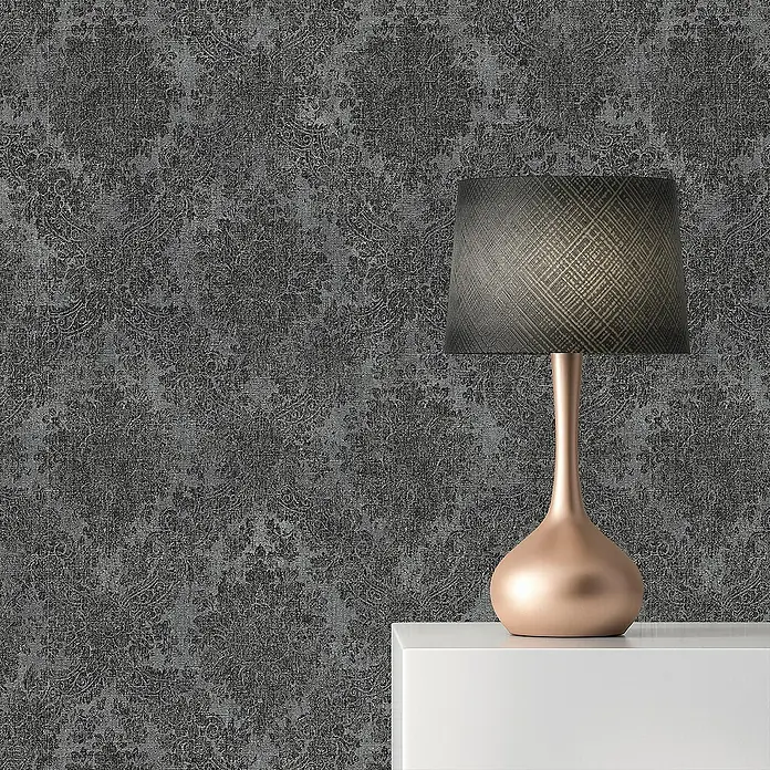 Tadessi Vliestapete M1-No.2431 - Schwarz, Ornament, 10,05 x 0,53 m - Dunkelgraue Tapete mit distressed Damastmuster, gezeigt mit einer roségoldenen Tischlampe.