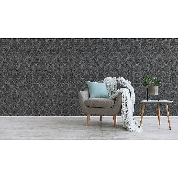 Tadessi Vliestapete M1-No.2431 - Schwarz, Ornament, 10,05 x 0,53 m - Dunkelgraue gemusterte Tapete an einer Wand hinter einem Sessel und Beistelltisch.