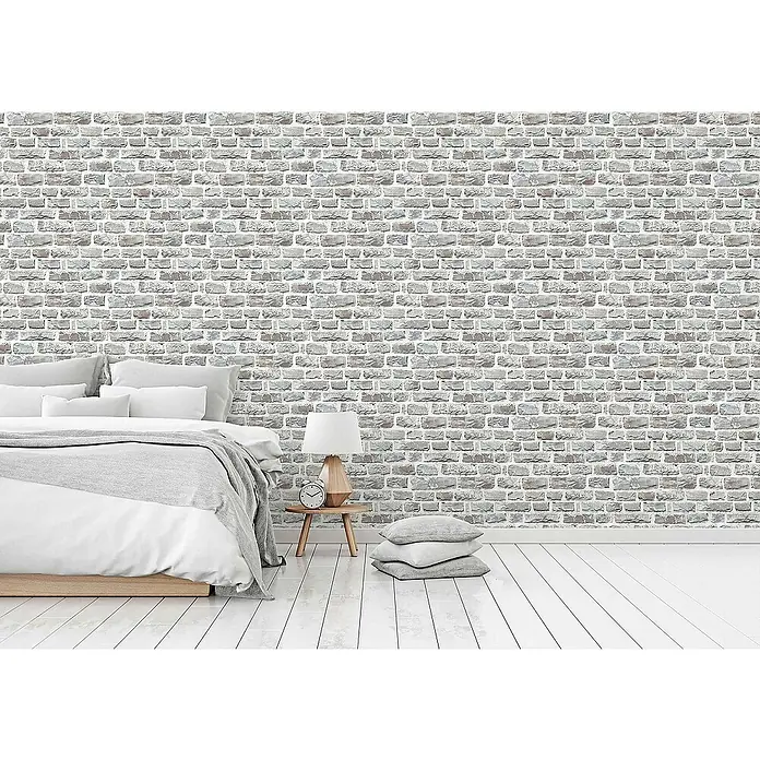 Tadessi Vliestapete M1-No.161 - Mehrfarbig, Steinoptik, 10,05 x 0,53 m - Grau-weiße strukturierte Ziegelstein-Tapete in einem Schlafzimmer hinter Bett und Nachttisch angebracht.