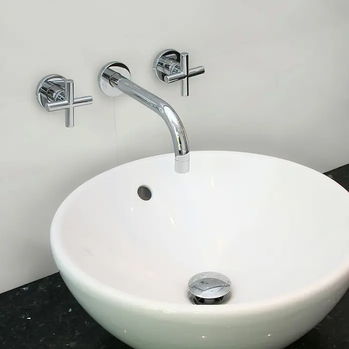 Revêt Wandpaneel SPC Wall - 600 x 300 mm, Weiß, Hochglänzend - Nahaufnahme eines modernen Waschbeckens mit einem eleganten Chromhahn und Kreuzgriffen an einer weißen Wand.