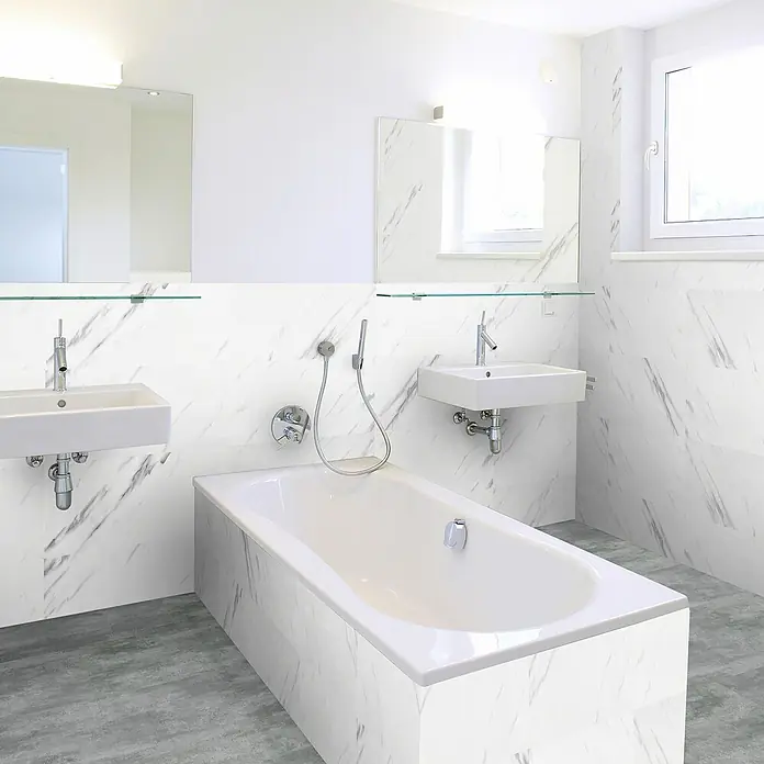 Revêt Wandpaneel SPC Wall - 600 x 300 mm, Marmor Weiß, Hochglänzend - Modernes Badezimmer mit Badewanne, zwei Waschbecken und Spiegeln. Helle, marmorierte Wände und grauer Boden sorgen für ein elegantes Ambiente.