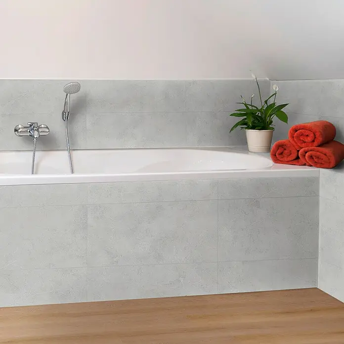 Revêt Wandpaneel SPC Wall - 600 x 300 mm, Grau - Das Foto zeigt eine Badewanne mit grauen Fliesen, Armaturen und einem Duschkopf, ergänzt durch orangefarbene Handtücher und eine Pflanze.