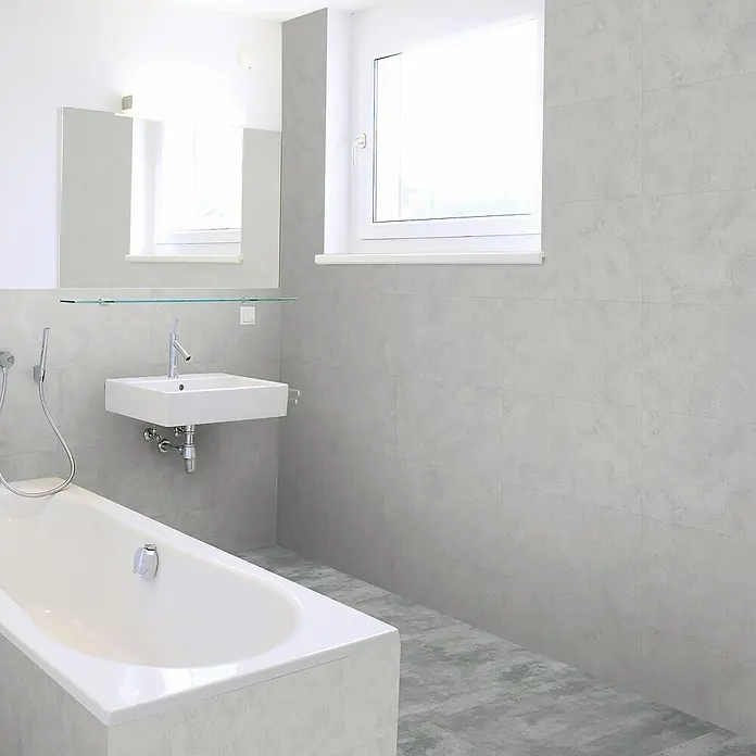 Revêt Wandpaneel SPC Wall - 600 x 300 mm, Grau - Helles Badezimmer mit weißer Badewanne, Waschbecken und Spiegel. Die Wand- und Bodenfliesen sind in einem dezenten Grauton gehalten und passen gut zusammen.