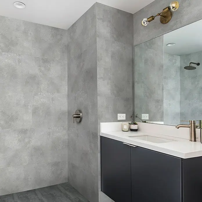 Revêt Wandpaneel SPC Wall - 600 x 300 mm, Beton Grau - Graues Badezimmer mit moderner Waschtischkombination mit weißen Arbeitsplatten und messingfarbenen Armaturen, dazu eine stilvolle Wandleuchte.