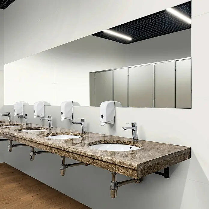Revêt Wandpaneel SPC Wall - 1.200 x 600 mm, Weiß, Hochglänzend - Eine öffentliche Toilette mit Waschbecken aus Marmor und einem großen Spiegel, der die Kabinen reflektiert.