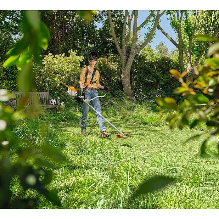 Stihl AK Akku-Motorsense FSA 80 GR. GSB 230-2 - 36 V, Ohne Akku, Schnittbreite Messer: 38 cm - Eine Frau benutzt einen STIHL Freischneider im Garten, um das Gras zu trimmen. Ideal für Gartenarbeit und Landschaftspflege.