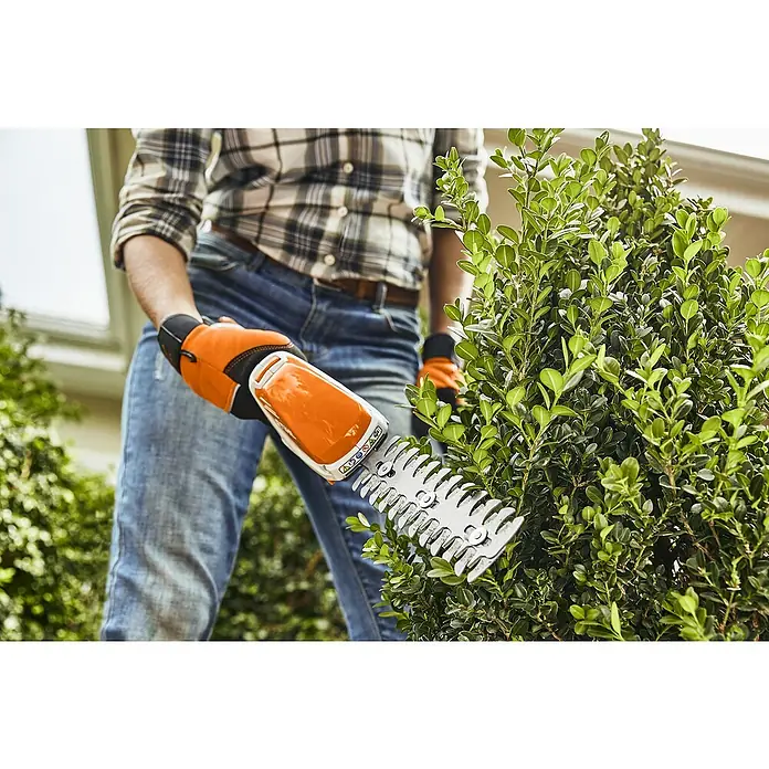 Stihl AS Akku-Gras- & Strauchschere HSA 26 - Li-Ionen, 1 Akku, Max. Aststärke: 19 mm - Ein Mann schneidet eine grüne Hecke mit einer akkubetriebenen STIHL HSA 25 Heckenschere mit Akku und orangefarbenen Handschuhen.