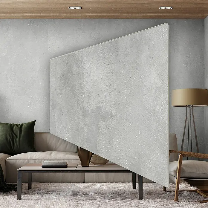 Revêt Wandpaneel SPC Wall - 1.200 x 600 mm, Beton Grau - Graue Sichtschutzwand aus Beton als Raumteiler im Wohnbereich mit Sofa, Tisch und Lampe, ideal für moderne Interieurs.