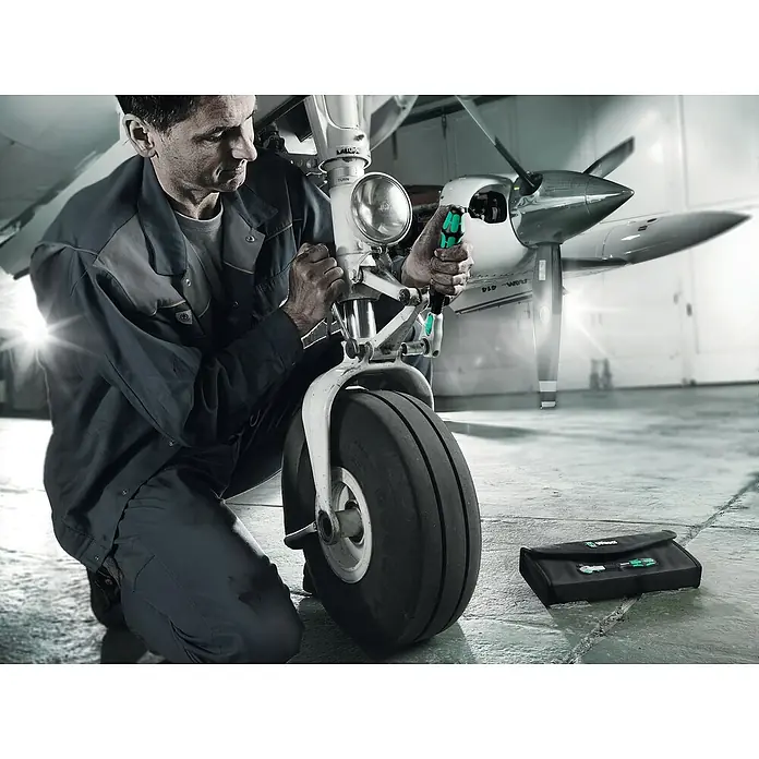 Wera Zyklop Knarre 8000 B Zyklop Speed Black Edition - ⅜″ - Flugzeugmechaniker bei der Arbeit mit Wera-Werkzeugen an einem Flugzeugfahrwerk. Ein Werkzeugsatz von Wera liegt daneben.