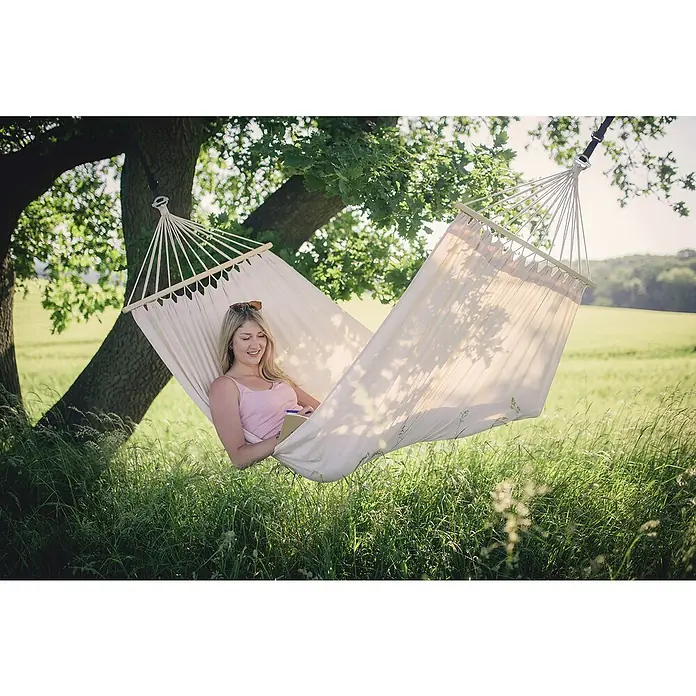 Amazonas Hängemattengestell Kronos - L x B x H: 358 x 113 x 105 cm, Holz, Naturbraun - Frau entspannt in einer Hängematte im Freien und liest ein Buch. Die Hängematte lädt zum Verweilen und Entspannen ein.
