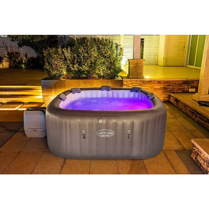 Bestway Lay-Z-Spa Mobil-Whirlpool Copenhagen Hydrojet - L x B x H: 201 x 201 x 80 cm, Grau, 1.050 l - Ein aufblasbarer Lay-Z-Spa Whirlpool mit lila beleuchtetem Wasser steht auf einer Terrasse und lädt zum Entspannen ein.