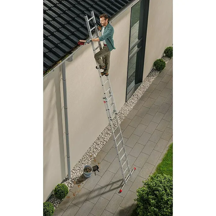Hailo Schiebeleiter S80 ProfiStep duo 2x9 Sprossen - Anzahl Tritte: 18 Stk., Arbeitshöhe: 514 cm, Belastbarkeit: 150 kg, Aluminium - Mann reinigt Dachrinne mit einer Mehrzweckleiter. Die Leiter ist stabil und vielseitig einsetzbar für Haus und Garten.