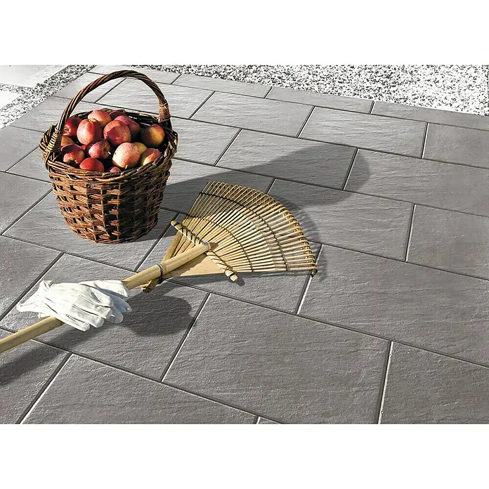 Diephaus Terrassenplatte Rancho - 60 x 30 x 4 cm, Mittelgrau, Beton - Nahaufnahme eines Korbs voller Äpfel, eines Rechens und eines Gartenhandschuhs auf einer grauen Steinterrasse.
