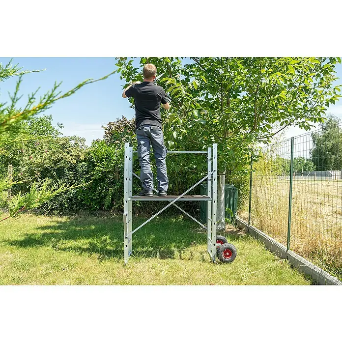 Hailo Leitergerüst HobbyStep H3 - Arbeitshöhe: 300 cm, Breite Plattform: 100 cm, Länge Plattform: 45 cm - Mann auf einem Gerüst im Garten, der einen Baum beschneidet. Das Gerüst hat Räder und ist aus leichtem Metall.