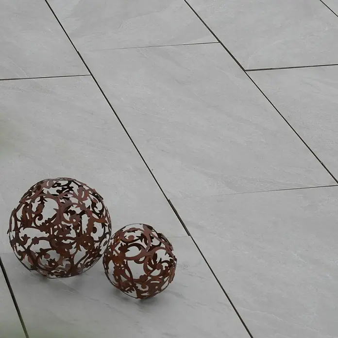 Diephaus Terrassenplatte Columbia - 80 x 40 x 4 cm, Core Quarz, Beton - Dekorative Kugeln: Zwei verschnörkelte Kugeln in verschiedenen Größen zieren einen hellen Fliesenboden und verleihen dem Raum eine elegante Note.