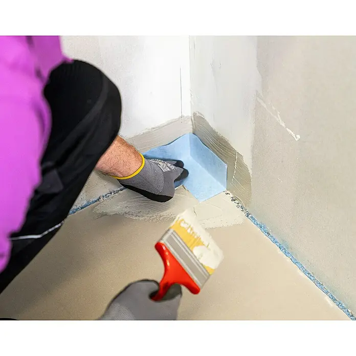 PCI Pecitape Dichtecke 90° Innen - Innenecke, 1 Stk. - Ein Handwerker, der eine Ecke abdichtet, mit einer blauen Dichtung und einem Pinsel, um eine wasserdichte Barriere zu schaffen.