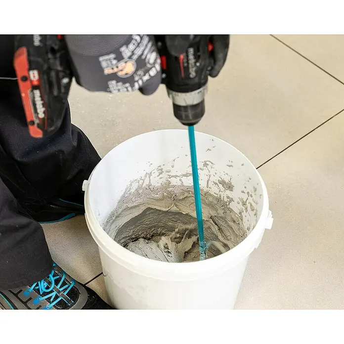 PCI Fugenmörtel Nanofug - Weiß, 4 kg - Ein Arbeiter mischt Mörtel in einem weißen Eimer mit einem Metabo-Bohrer und einem blauen Rührwerk, um Fliesen zu verlegen.