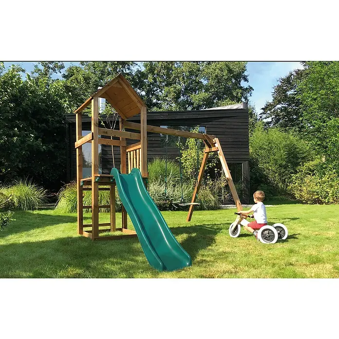Soulet Kinderspielturm Noumea - L x B x H: 2.730 x 3.130 x 2.370 mm, Holz - Ein hölzernes Klettergerüst mit Rutsche und Schaukel steht auf einem Rasen mit einem Kind auf einem Dreirad.