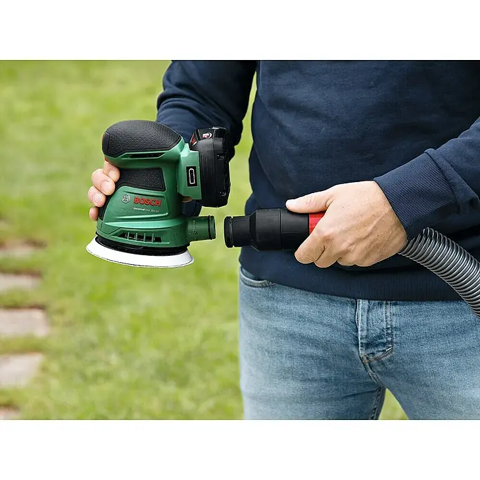Bosch Power for All 18V Akku-Exzenterschleifer UniversalOrbit 18V-20 - 18 V, Ohne Akku, Durchmesser Schleifteller: 125 mm - Ein Mann schließt eine Schleifmaschine von Bosch an einen Staubsaugerschlauch an. Das Elektrowerkzeug ist in Grün und Schwarz gehalten.