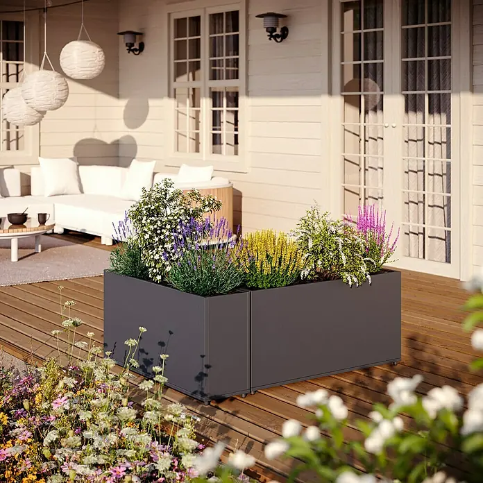 Sunfun Lumar Pflanzkübel eckig - Außenmaß (L x B x H): 89 x 23 x 45 cm, Stahl, Night-Grey - Der dunkle Blumenkasten mit verschiedenen Pflanzen steht auf einer Terrasse mit Holzboden vor einem Haus.