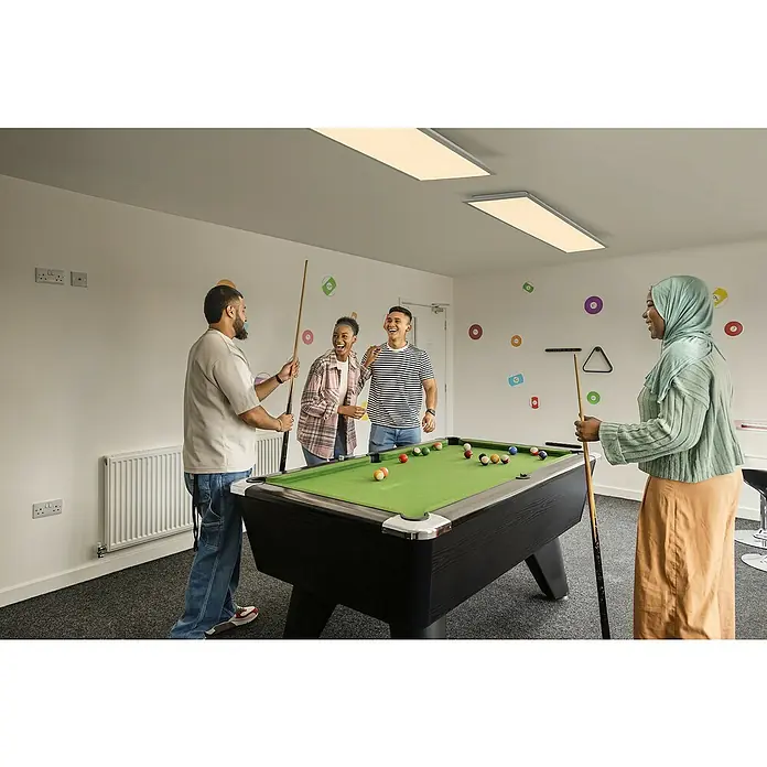 Osram Smart+ LED-Panel Planon Magic RGB + Tunable White - 36 W, L x B x H: 119,5 x 29,5 x 6 cm, Weiß, RGBW - Billardtisch-Szene: Eine Gruppe von Freunden genießt ein Billardspiel in einem hellen, modernen Raum. Der Fokus liegt auf dem Billardtisch.