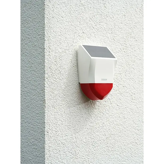 Osram Smart+ Alarmsirene - Außen, 95 dB, Batteriebetrieben - Nahaufnahme einer Osram-Alarmsirene mit Solarpanel an einer weißen Wand.