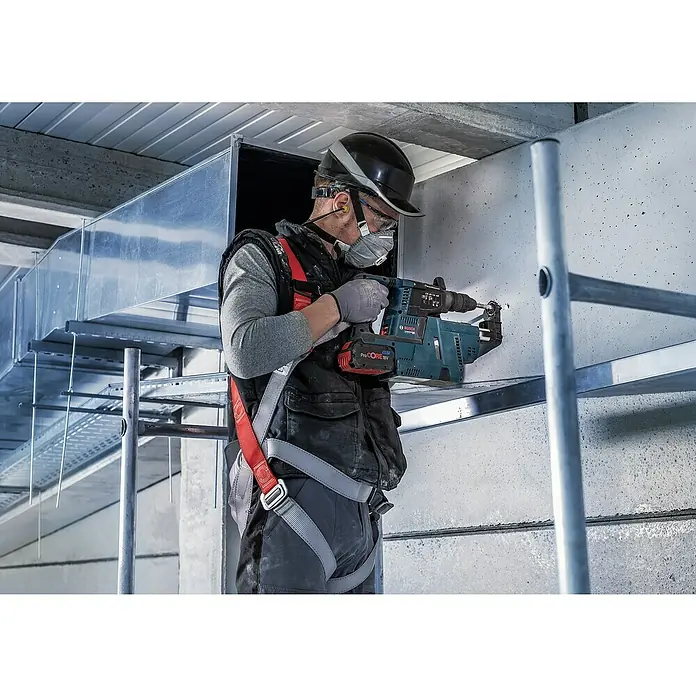 Bosch Beton- & Steinbohrer PRO SDS plus-5X - 1 Stk., Durchmesser Bohrer: 14 mm, Arbeitslänge: 200 mm - Ein Bauarbeiter mit Schutzhelm und Atemschutzmaske bohrt mit einer Bosch-Bohrmaschine ein Loch in eine Wand. Er trägt Sicherheitsausrüstung.