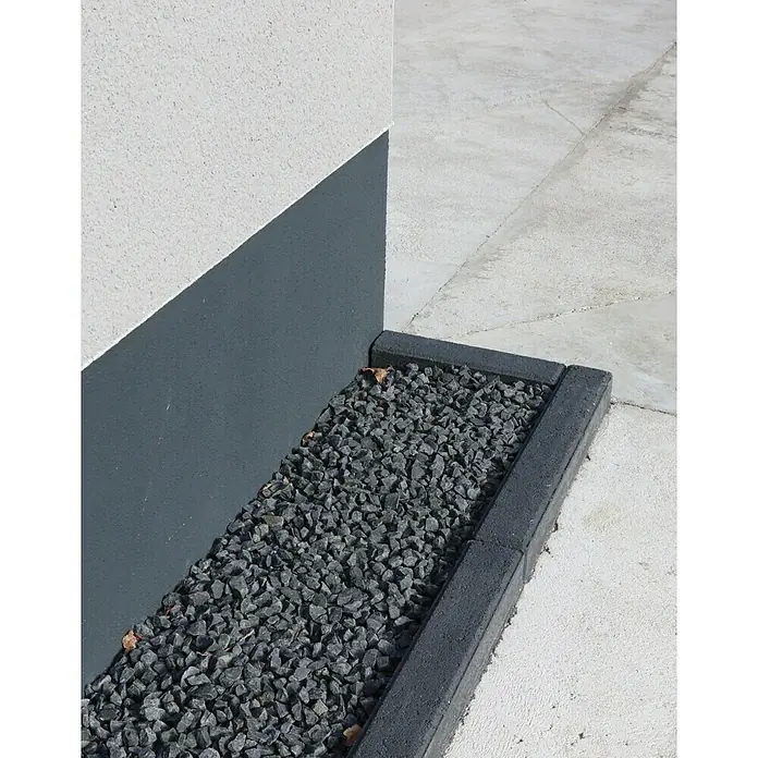 Christoph Randstein - 100 x 7 x 17 cm, Anthrazit, Beton - Nahaufnahme eines Zierkiesbeets mit grauen Steinen und einer dunklen Bordsteinkante vor einer Hauswand.