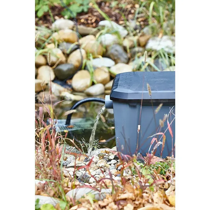 Heissner Durchlauffilter-Set - 33 W, Teichgröße: 8.000 l - Teichfilter von Heissner im Einsatz, umgeben von Steinen und Pflanzen. Das klare Wasser fließt zurück in den Teich und sorgt für sauberes Wasser.