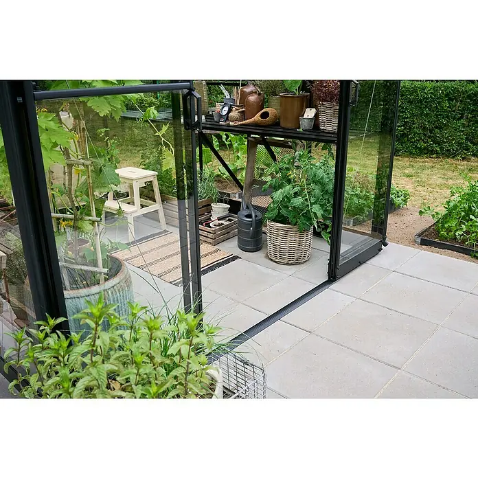 Halls Gewächshaus Qube Square - Außenmaß inkl. Dachüberstand (B x T): 250,8 x 250,8 cm, Material Seitenwand: Glas, 3 mm, Schwarz - Ein Gewächshaus mit geöffneter Tür zeigt Pflanzen wie Tomaten und Kräuter, die auf einem Regal und in Töpfen wachsen, umgeben von grauem Steinboden.