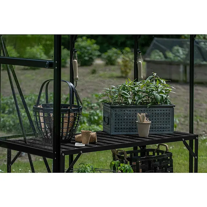 Halls Gewächshaus-Tisch 1 - 120,8 x 76 cm, Schwarz, Doppelte Ablageebene - Nahaufnahme eines Gewächshaustisches mit Pflanzen, Körben und Gartengeräten, der eine ruhige Gartenszene zeigt.