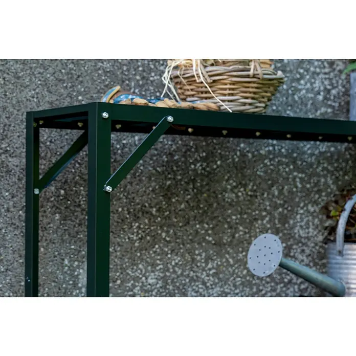 Halls Aufsatz für Gewächshaus-Tisch - 120,8 x 26 x 3,7 cm, Grün, Passend für: Halls Tische ( 1 Ablagefläche) - Nahaufnahme eines dunkelgrünen Gartentisches mit Ablagefläche, auf der ein Korb und eine Dekofigur stehen, im Hintergrund eine Gießkanne.
