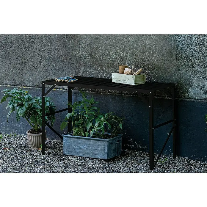 Halls Gewächshaus-Tisch 1 - 120,8 x 76 cm, Schwarz, Doppelte Ablageebene - Ein schwarzer Gartentisch mit Pflanzen und Gartengeräten vor einer Wand. Der Tisch bietet Ablagefläche für Pflanzen und Werkzeuge.