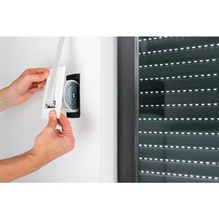 Schellenberg Rollladen-Gurtwickler Maxi - Lochabstand: 105 mm, Gurtbreite: 23 mm, Max. Gurtlänge: 5 m - Nahaufnahme einer Person, die eine weiße Abdeckung an einem Rollladengurtwickler an einer Wand befestigt.