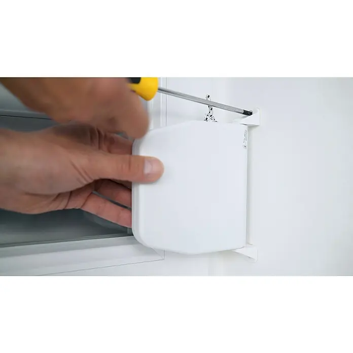 Schellenberg Rollladen-Gurtwickler - Aufputz, Lochabstand: 155 mm - Eine Person befestigt einen weißen Rollladen mit einem gelben Schraubenzieher an einem weißen Fensterrahmen. Der Rollladen ist quadratisch und modern.