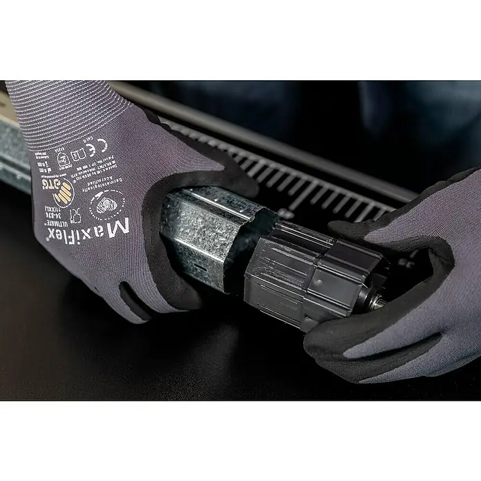 Schellenberg Walzenhülse Maxi - Durchmesser Achtkantwelle: 60 mm, Länge: 72 mm, Geeignet für: Rollladen-Maxi-Systeme - Eine Nahaufnahme von Händen mit Maxiflex-Handschuhen, die ein Metallteil an einem schwarzen Bauteil befestigen.