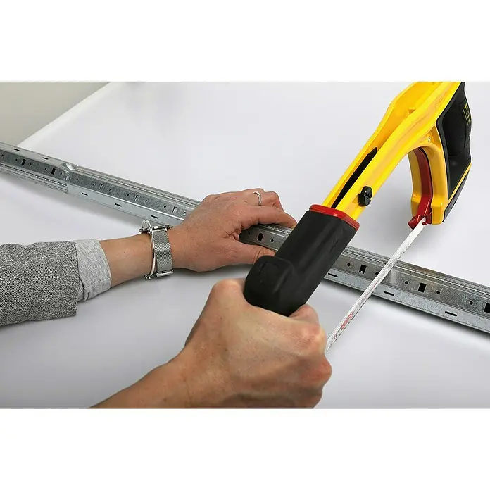 Schellenberg Achtkantwellen-Set Mini - Auszugslänge: 130 cm, Geeignet für: Rollladen-Mini-Systeme - Eine Person benutzt eine Metallsäge mit gelbem Griff, um ein Metallstück zu schneiden.