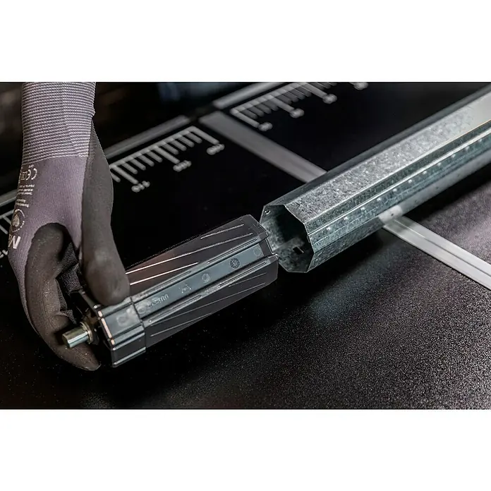 Schellenberg Walzenhülse Maxi - Durchmesser Achtkantwelle: 60 mm, Länge: 150 mm, Geeignet für: Rollladen-Maxi-Systeme - Eine Hand mit Handschuh setzt ein schwarzes Rollo-Endstück in ein verzinktes, sechseckiges Rohr ein. Das Produkt liegt auf einer schwarzen Oberfläche mit Maßeinteilung.
