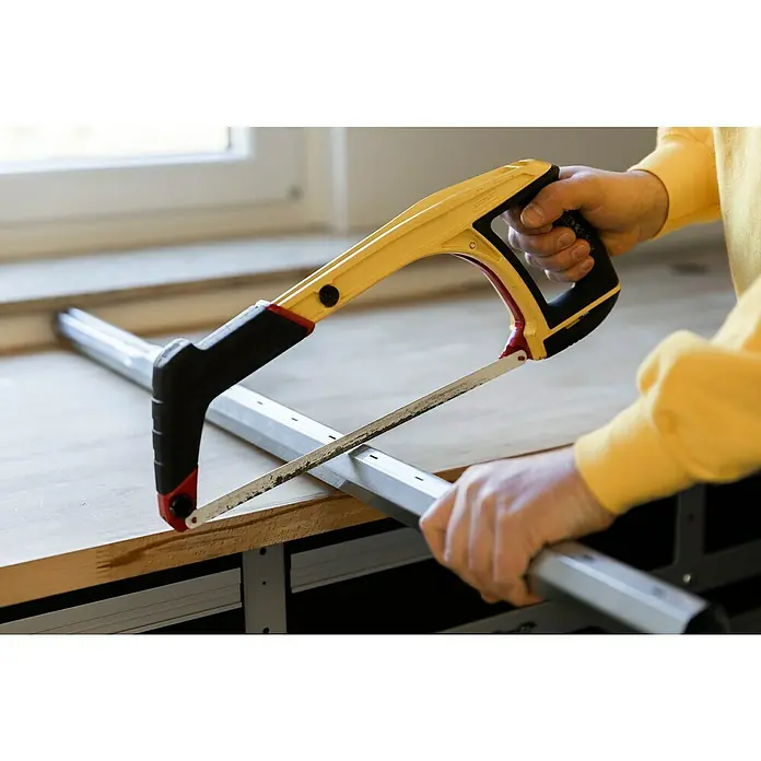 Schellenberg Teleskop-Achtkantwelle Mini - Geeignet für: Rollladen-Mini-Systeme - Handwerker sägt ein Metallrohr mit einer Bügelsäge. Die gelbe Bügelsäge wird von beiden Händen gehalten, während die Säge das Rohr durchtrennt.