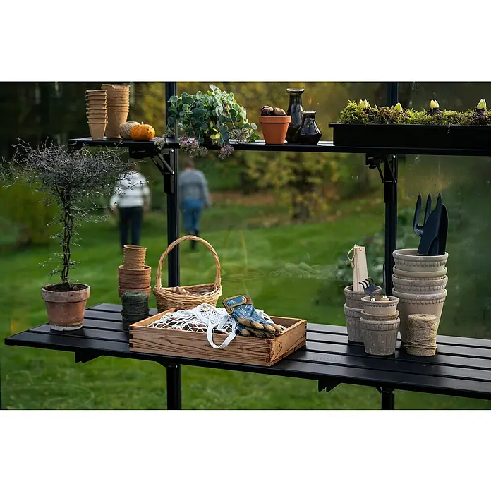 Juliana Gewächshaus-Regal - 235 x 21,8 cm, Schwarz - Gartenszene mit Pflanzentisch: Töpfe, Werkzeuge, Pflanzen und Gartenhandschuhe auf einem schwarzen Tisch mit Regalen im Gewächshaus.