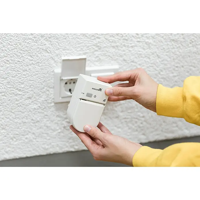 Schellenberg Smart Home Funksteckdose - Außen, Weiß - Eine Hand hält einen Schellenberg Rolladen Zeitschaltuhr in der Nähe einer Steckdose. Das Gerät ist weiß und hat ein einfaches Design.