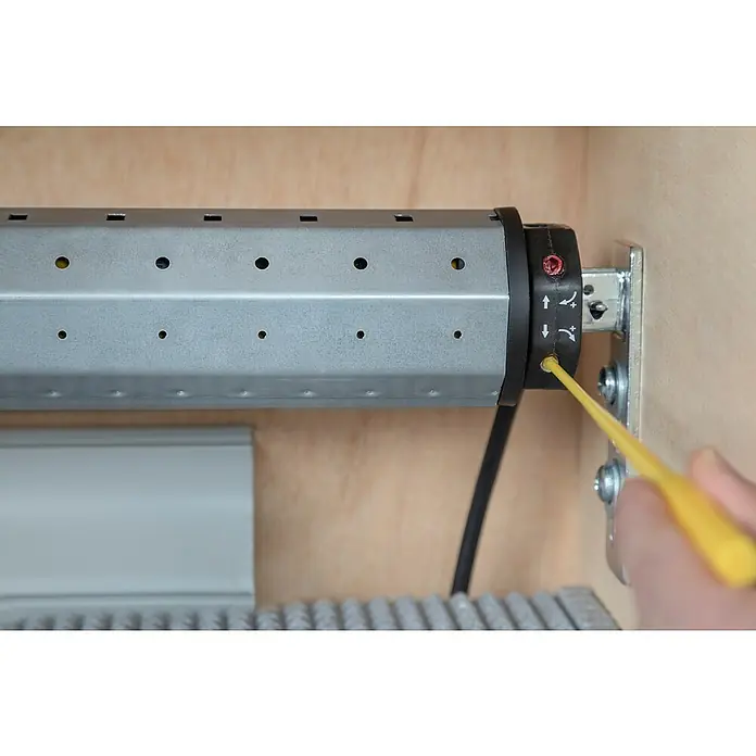 Schellenberg Rohrmotor Rollopower Action Maxi 6 - Max. Rollladenfläche: 3 m² bei Kunststoffrollläden, Einbaulänge: 500 mm, Zugkraft: 15 kg - Eine Nahaufnahme einer Rollladensteuerung, die mit einem gelben Werkzeug justiert wird. Fokus liegt auf dem Einstellmechanismus.