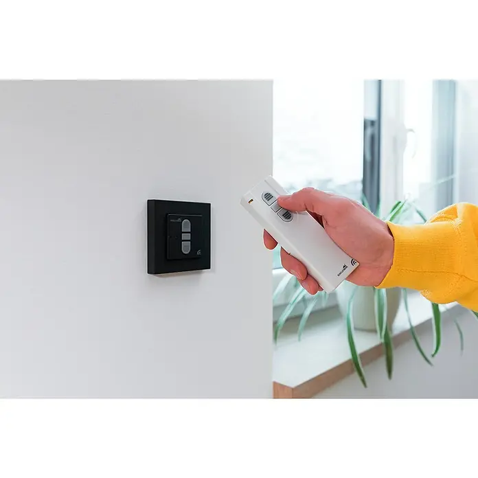 Schellenberg Smart Home Funk-Empfangsschalter - 40 x 80 x 80 mm, Anthrazit, Unterputzmontage - Ein Mann bedient eine Schellenberg Funksteuerung zur Steuerung von Rollläden. Die Steuerung ist weiß und hat drei Knöpfe.