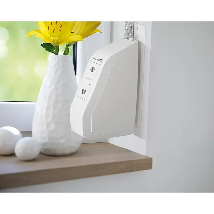 Schellenberg Funk-Rollladen-Gurtwickler Rollo Drive 75 Premium - L x B x H: 155 x 37 x 199 mm, Gurtbreite: 14 mm - 15 mm, Zugkraft: 30 kg, Unterstützte Systeme: Schellenberg Smart Home System - Nahaufnahme eines Schellenberg RolloDrive 75 elektronischen Gurtwicklers mit weißem Gehäuse und Bedienelementen an einer Fensterbank.