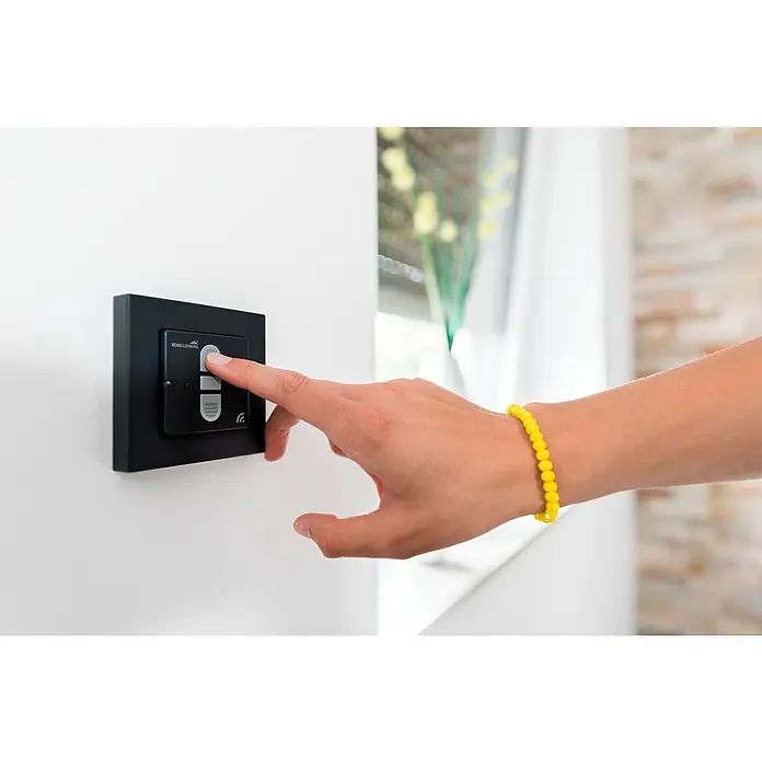 Schellenberg Smart Home Funk-Empfangsschalter - 40 x 80 x 80 mm, Anthrazit, Unterputzmontage - Nahaufnahme einer Person, die einen schwarzen Schellenberg-Schalter an einer weißen Wand betätigt, mit Fokus auf das moderne Design und die einfache Bedienung.