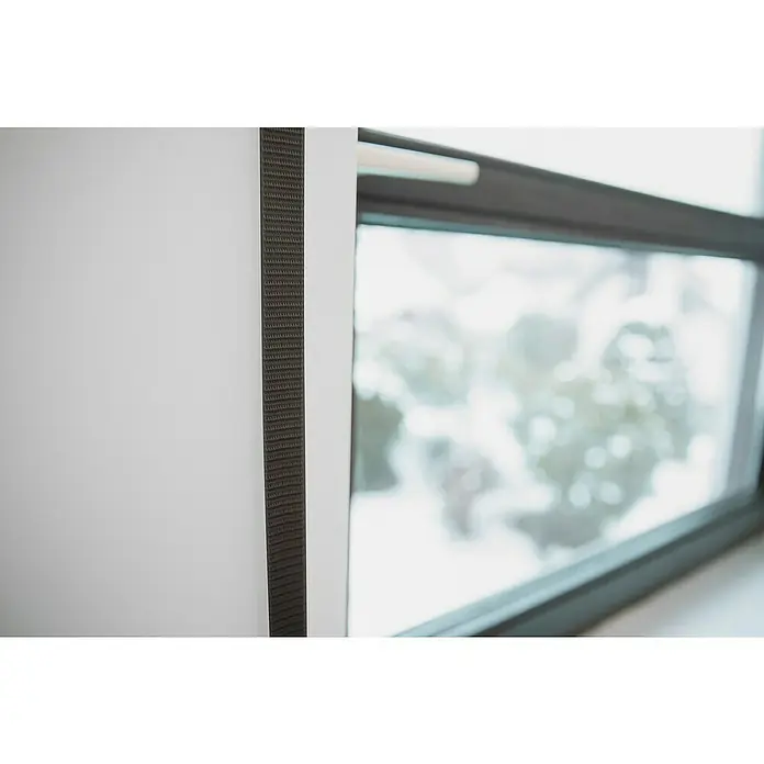 Schellenberg Rollladengurt - Braun, Länge: 6 m, Gurtbreite: 23 mm - Nahaufnahme einer Gardinenleiste in dunklem Grau vor einem Fenster, das einen verschneiten Außenbereich zeigt.