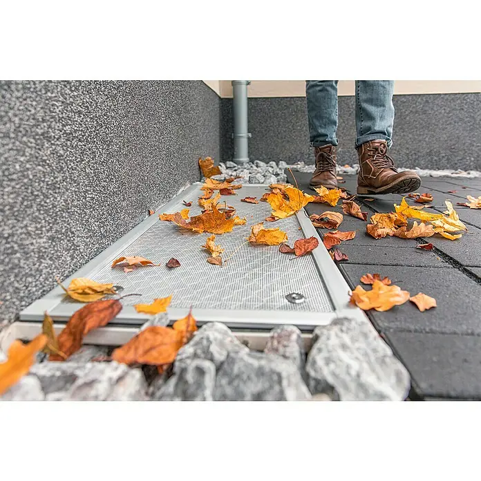 Schellenberg Lichtschachtabdeckung - B x H: 55 x 110 cm, Aluminium - Laub liegt auf einem modernen Lichtschachtgitter aus Metall, während eine Person mit Stiefeln darauf steht.