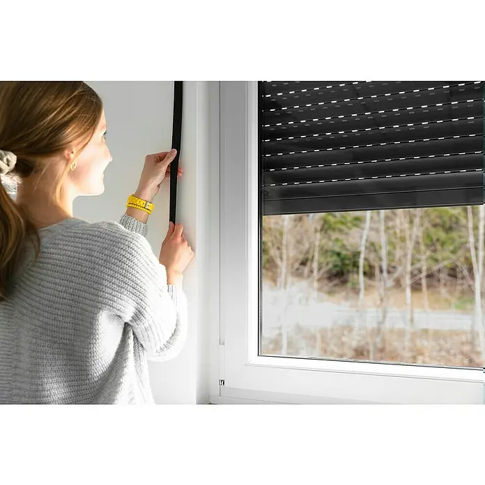 Schellenberg Rollladengurt - Schwarz, Länge: 6 m, Gurtbreite: 23 mm - Frau montiert Rollladen am Fenster. Der Rollladen bietet effektiven Sonnen- und Sichtschutz und trägt zur Energieeffizienz bei.